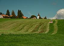 Blick zurück auf den Ausgangsort: Ein Bauer mäht das Gras auf deiner Wiese, im Hintergrund ist der Turm der Kirche Heimenschwand zu sehen.  (bei Klick vergrösserte Ansicht Bild)