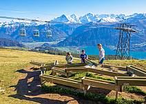 Zeit für Spiel und Spass beim grossen Alpenspielplatz mit der Holzkugelbahn; eine prächtige Aussicht inklusive. Im Hintergrund die Gondeln der Gruppen-Umlaufbahn auf  (bei Klick vergrösserte Ansicht Bild)